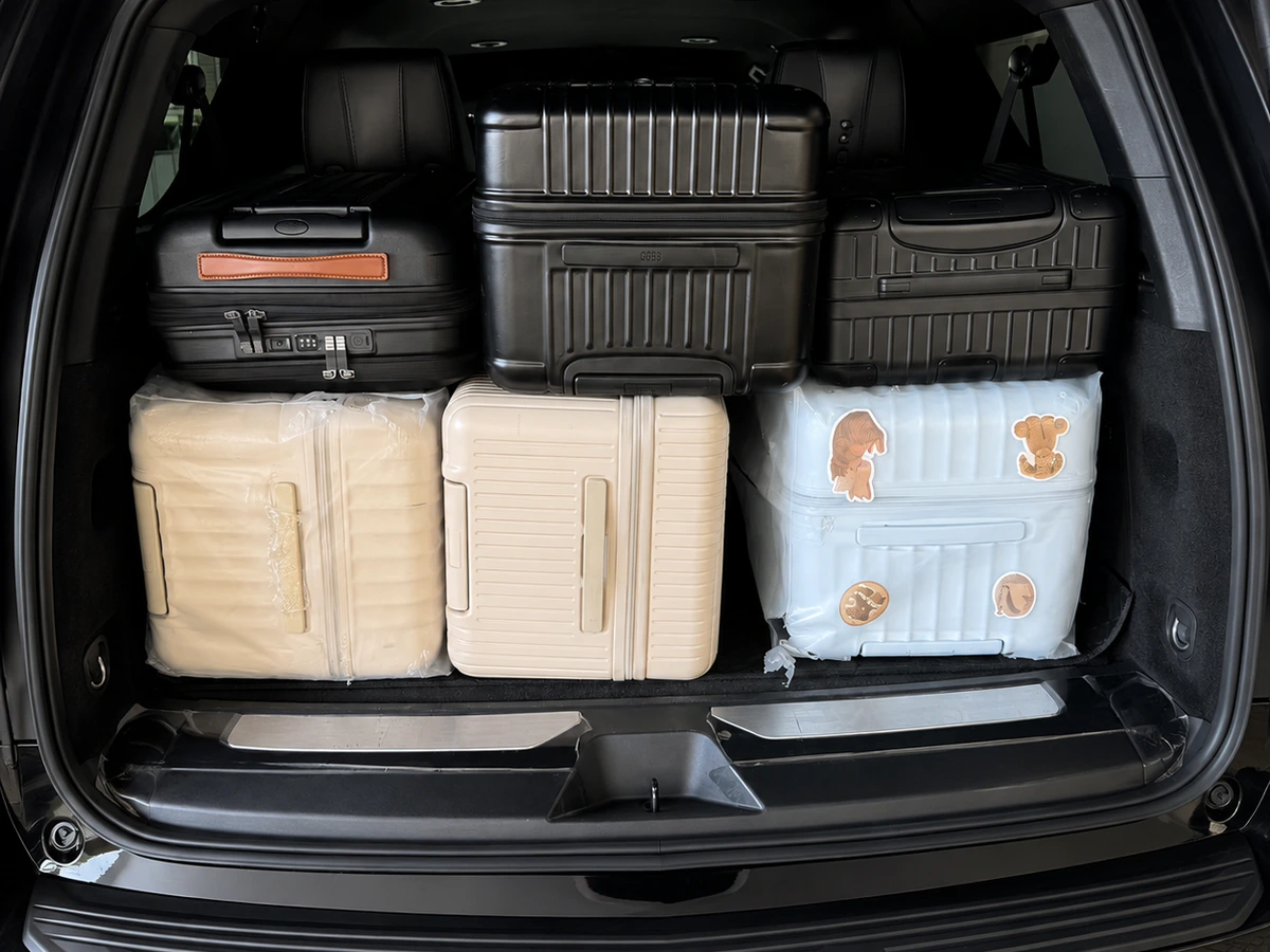 Open full-size black SUV trunk packed with six large suitcases